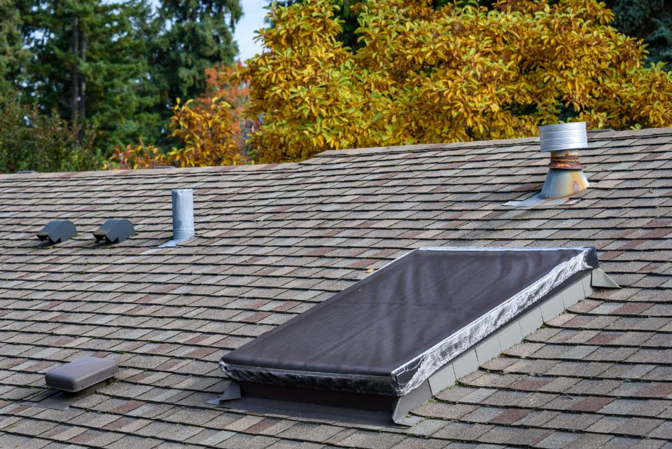 Suburban house rooftop, asphalt shingles, skylight with cover, roof vents